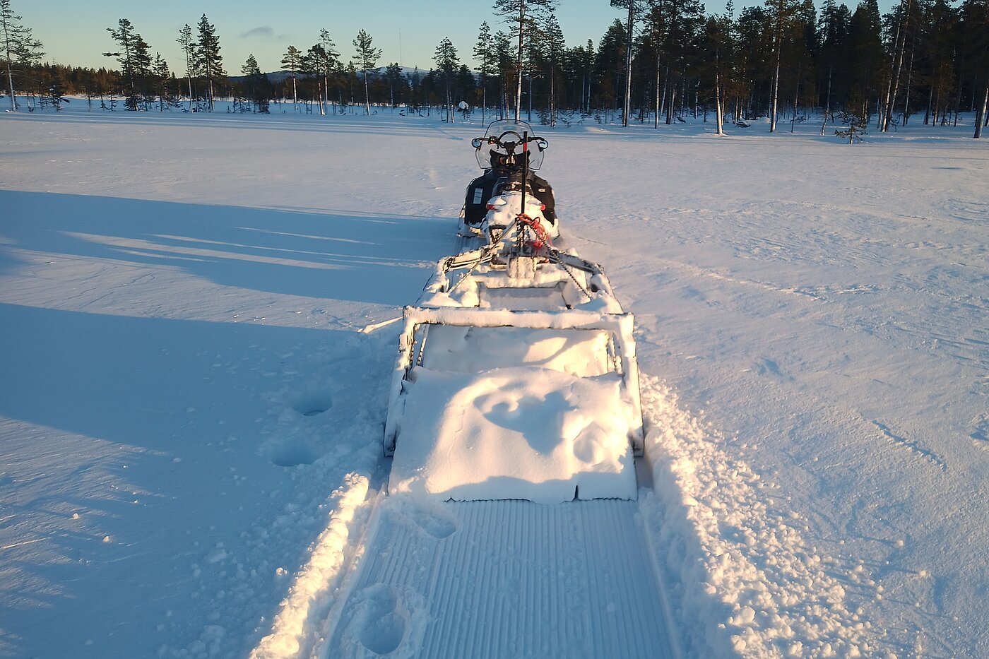Schneemobil präpariert Hundeschlitten-Route auf gefrorenem See Lappland