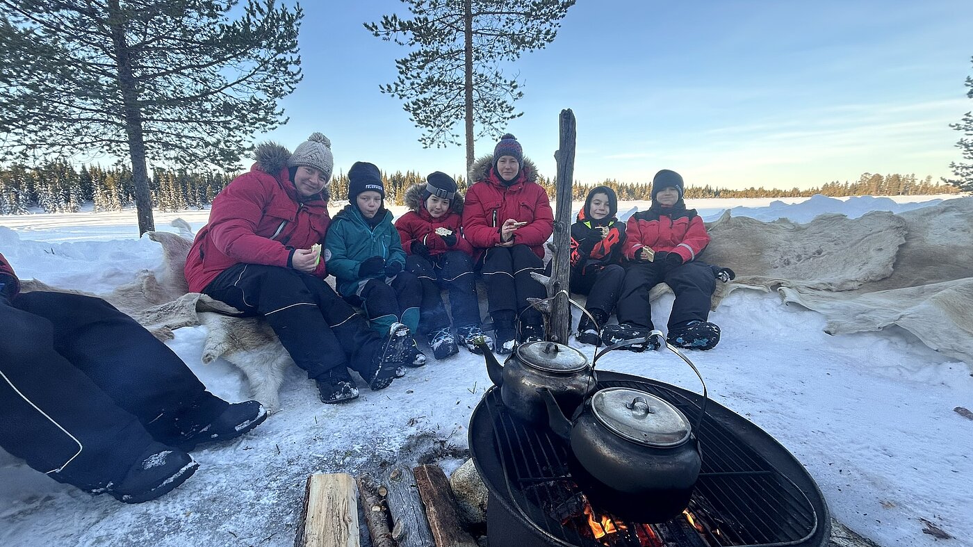 Familie am Lagerfeuer im Winterurlaub Lappland