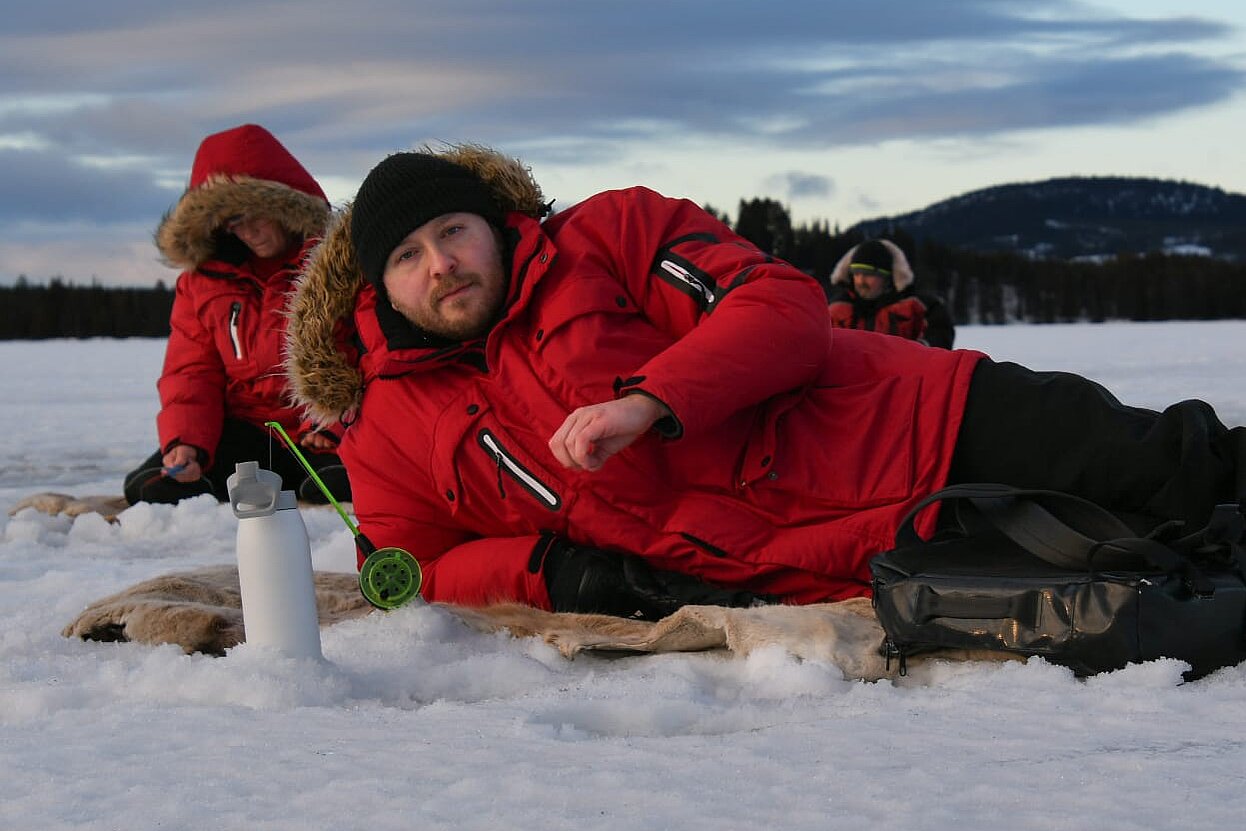 Gäste beim Eisangeln auf gefrorenem See in Lappland