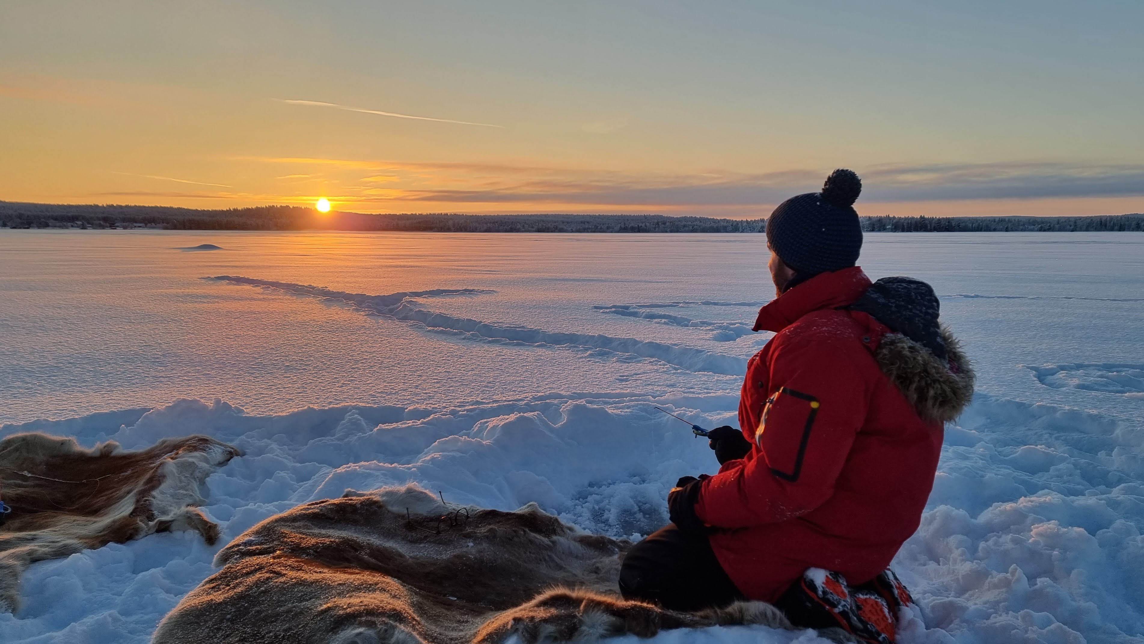 Person sitzt im Schnee und blickt auf Sonnenuntergang in Lappland